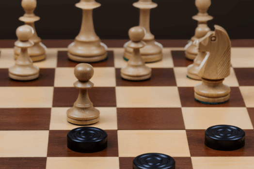 A chess board with chess pieces played against checkers pieces.